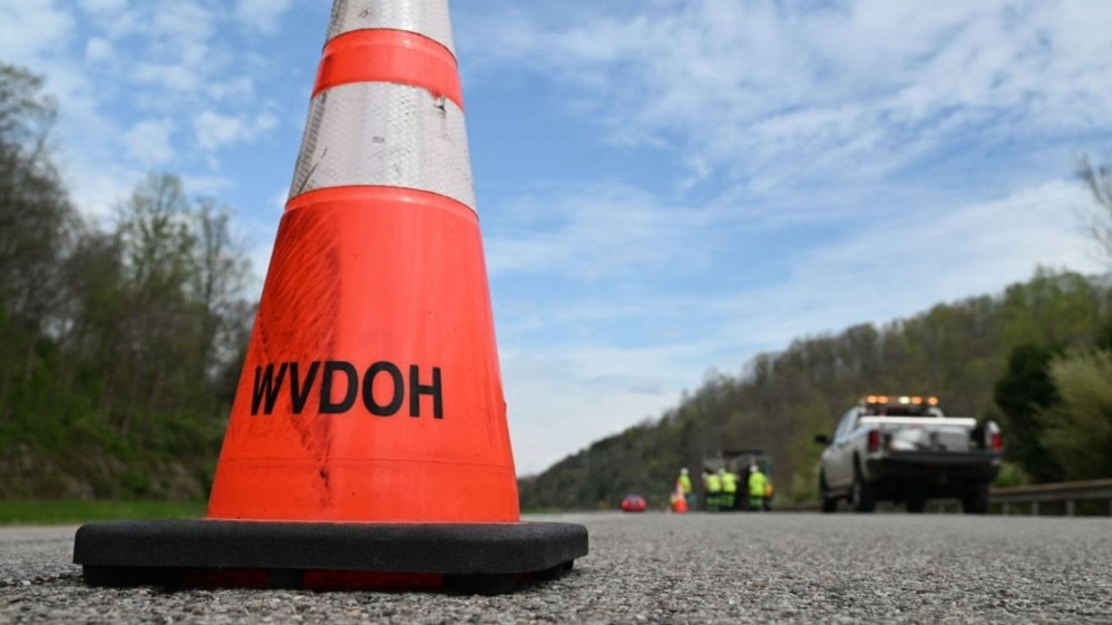 A DOH-branded traffic cone is seen in the foreground while workers complete a task in the background.