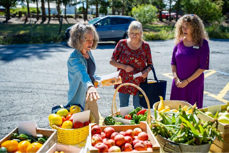 Three women browse through an assortment of vegetables at an outdoor market
